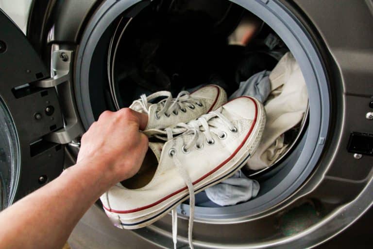 Main plaçant des baskets blanches dans un lave-linge avec du linge